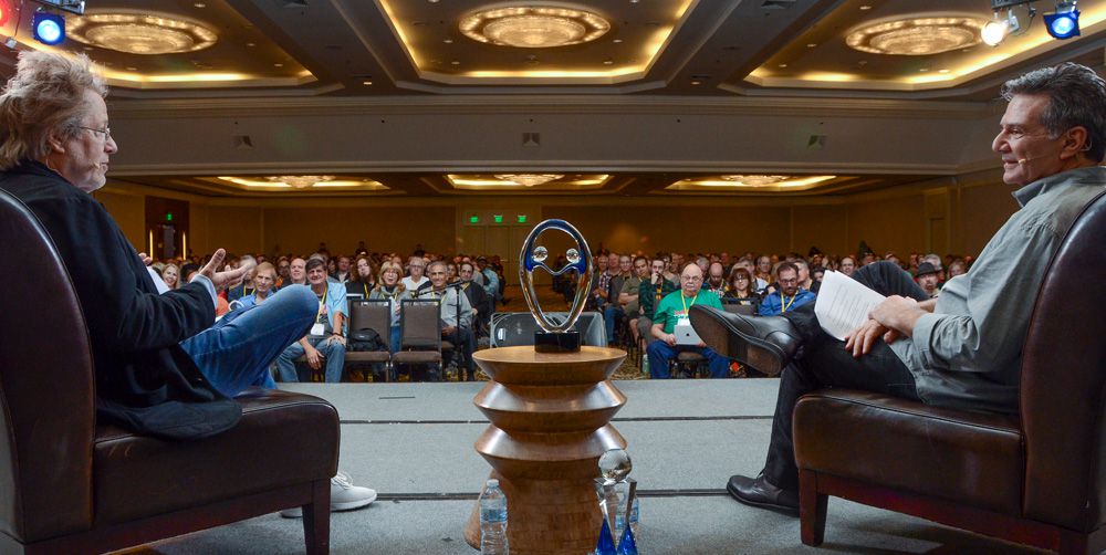 2 gentlemen sitting on the stage in-front of a crowd